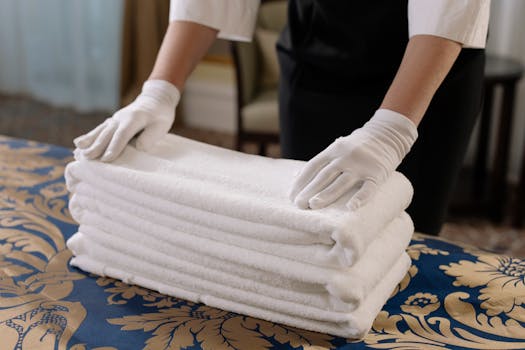 Professional housekeeper folding clean towels on a bed in a hotel room, emphasizing neatness and service.