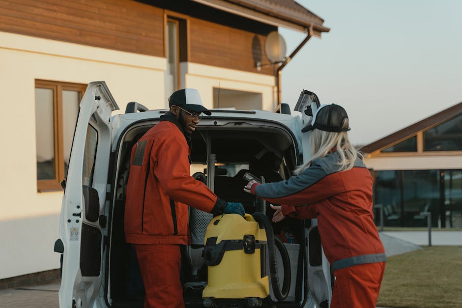 cleaning house service - Two cleaners in red uniforms load a vacuum into a white van outdoors.